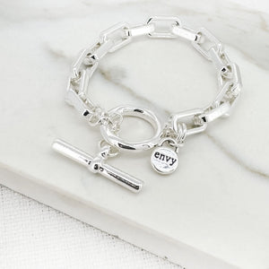 Silver bracelet with a round charm and 'envy' tag on a white surface