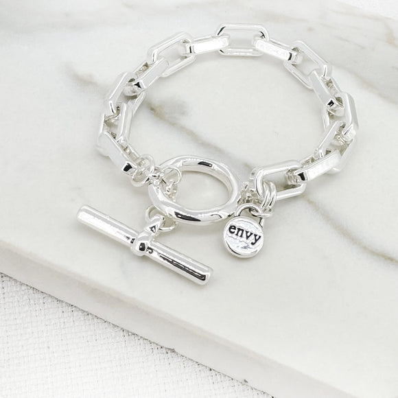 Silver bracelet with a round charm and 'envy' tag on a white surface